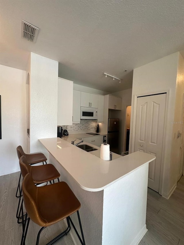 kitchen featuring white cabinetry, sink, backsplash, kitchen peninsula, and a breakfast bar area