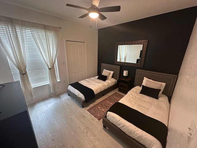 bedroom with light wood-type flooring, ceiling fan, and a closet