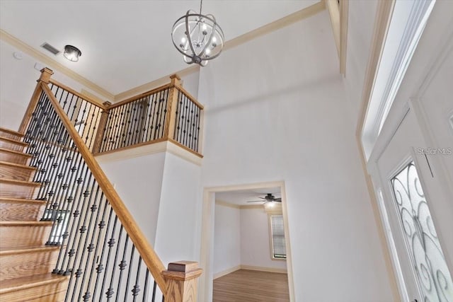 staircase featuring a towering ceiling, ceiling fan with notable chandelier, crown molding, and hardwood / wood-style flooring