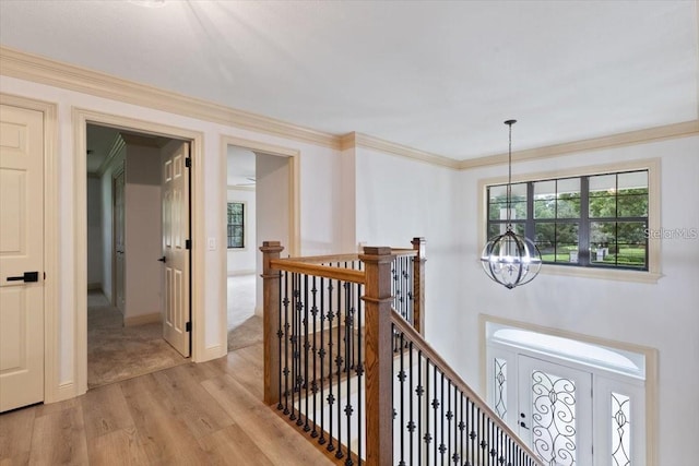 corridor with light hardwood / wood-style flooring, crown molding, and a notable chandelier