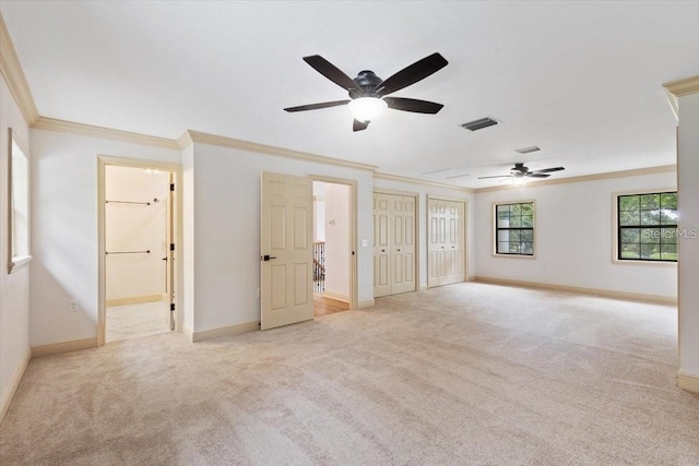 interior space featuring ceiling fan, light colored carpet, two closets, and crown molding