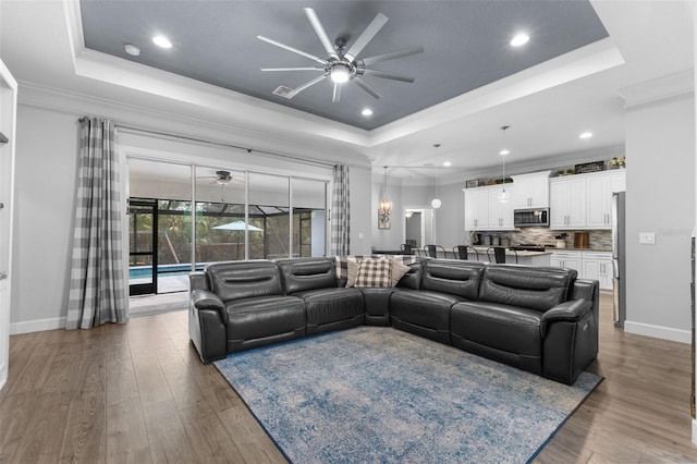 living room with ceiling fan, wood-type flooring, crown molding, and a tray ceiling