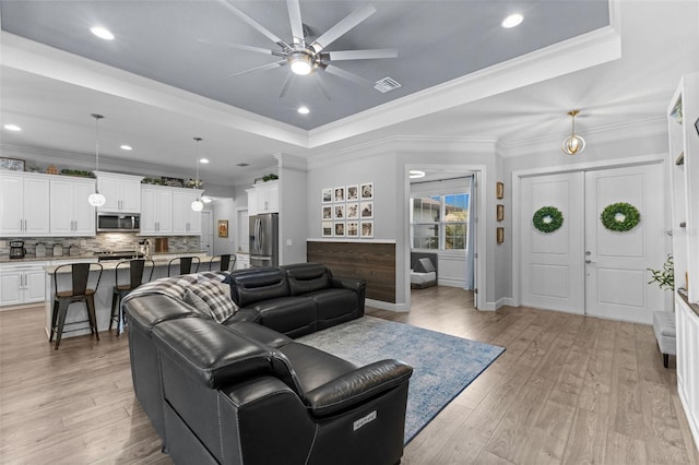 living room with ceiling fan, light wood-type flooring, a tray ceiling, and crown molding