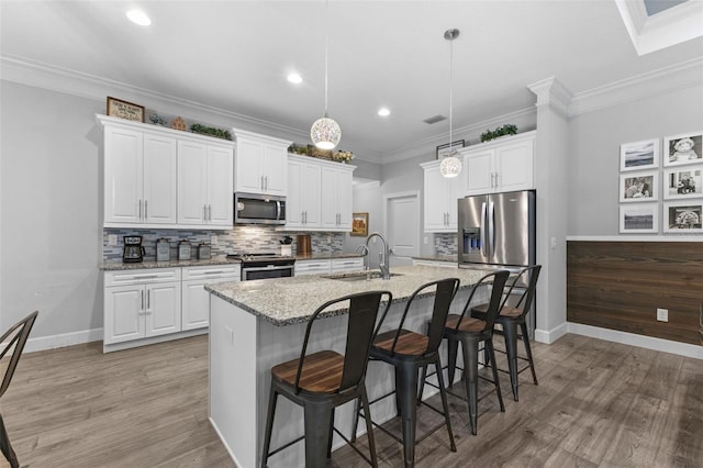 kitchen with white cabinetry, appliances with stainless steel finishes, a kitchen island with sink, light stone counters, and sink