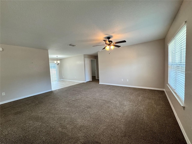 carpeted spare room featuring a wealth of natural light, ceiling fan with notable chandelier, and a textured ceiling