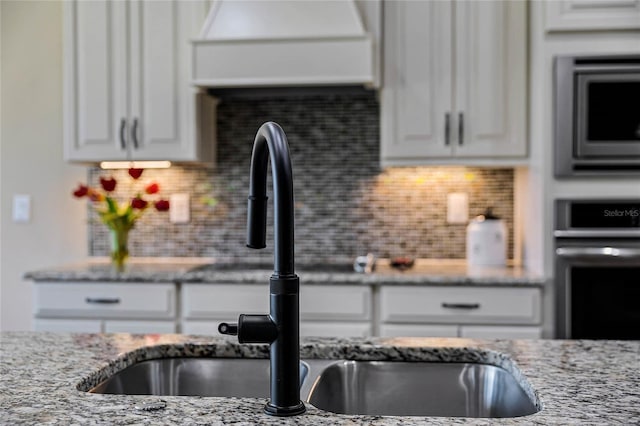 kitchen with light stone counters, backsplash, white cabinetry, and stainless steel appliances