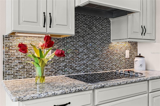 kitchen with tasteful backsplash, custom range hood, white cabinets, light stone counters, and black cooktop