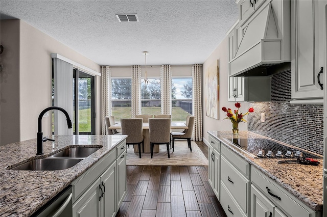 kitchen featuring light stone countertops, dishwasher, black electric stovetop, premium range hood, and sink