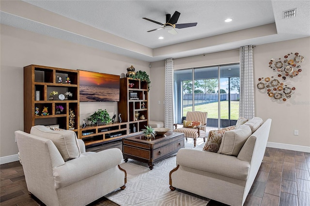 living room featuring ceiling fan, a tray ceiling, and a textured ceiling