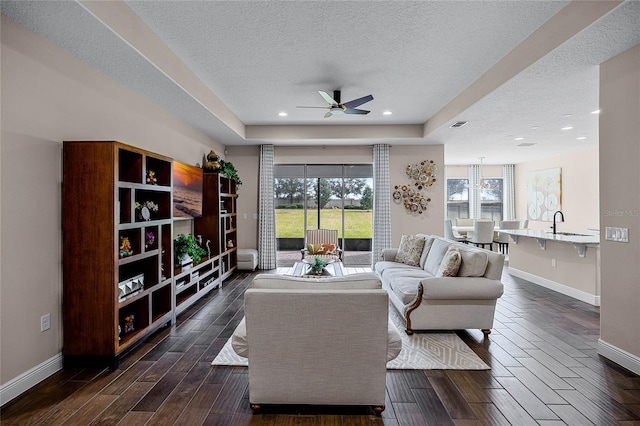 living room featuring ceiling fan, sink, a tray ceiling, and a textured ceiling