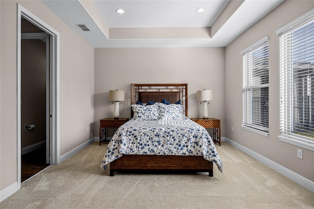 bedroom with light colored carpet and a tray ceiling