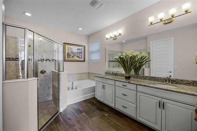 bathroom with a textured ceiling, vanity, and plus walk in shower