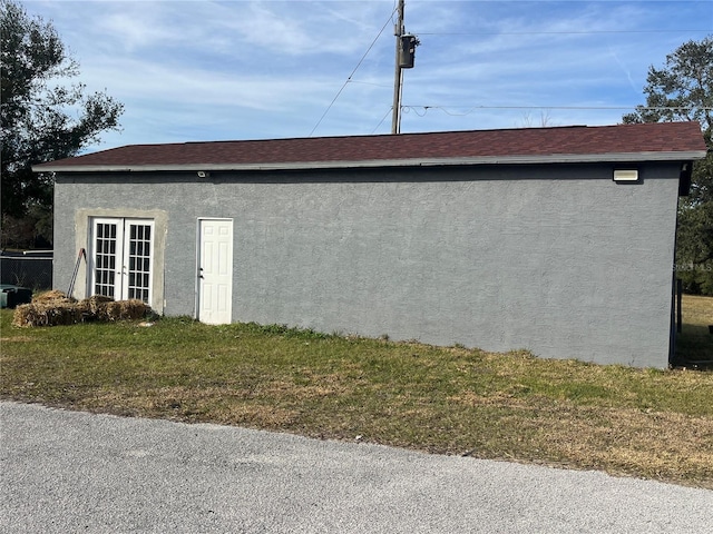 view of side of property featuring french doors, a shingled roof, and stucco siding