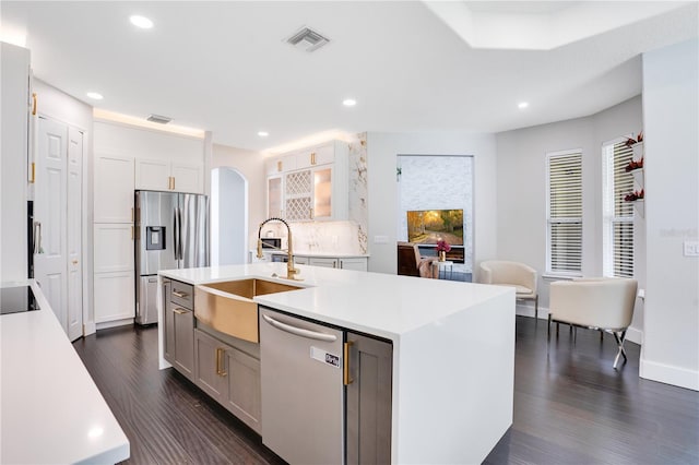 kitchen with dark wood-type flooring, sink, appliances with stainless steel finishes, an island with sink, and white cabinets