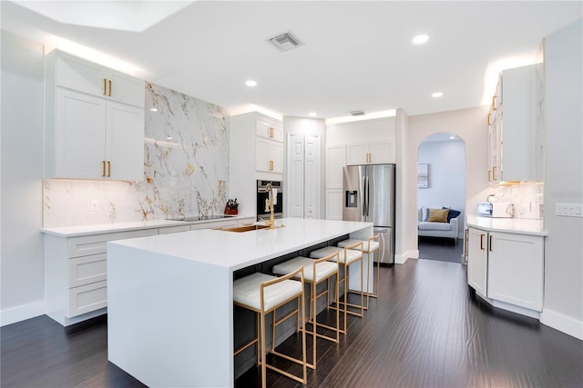 kitchen with dark wood-type flooring, a breakfast bar, appliances with stainless steel finishes, an island with sink, and white cabinets