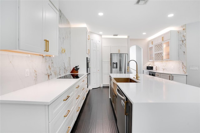 kitchen with tasteful backsplash, white cabinetry, a kitchen island with sink, stainless steel appliances, and dark wood-type flooring