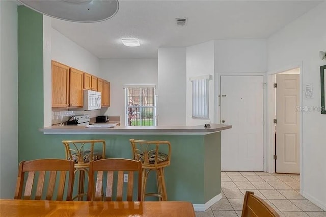 kitchen featuring electric stove, kitchen peninsula, decorative backsplash, a kitchen bar, and light tile patterned floors