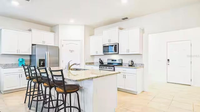 kitchen with white cabinetry, stainless steel appliances, sink, a kitchen island with sink, and light stone counters