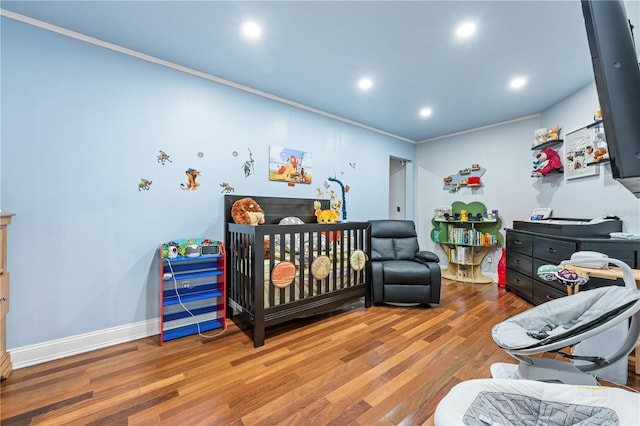 bedroom with hardwood / wood-style floors, ornamental molding, and a crib