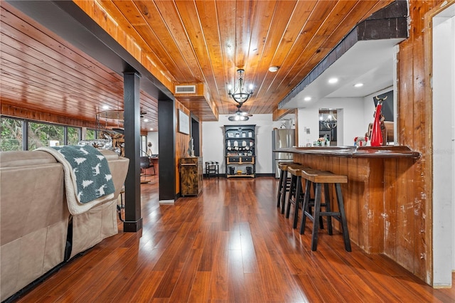 dining area featuring bar area, dark hardwood / wood-style flooring, wood ceiling, and an inviting chandelier