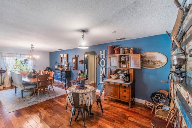 dining area featuring a textured ceiling, dark hardwood / wood-style flooring, and a chandelier