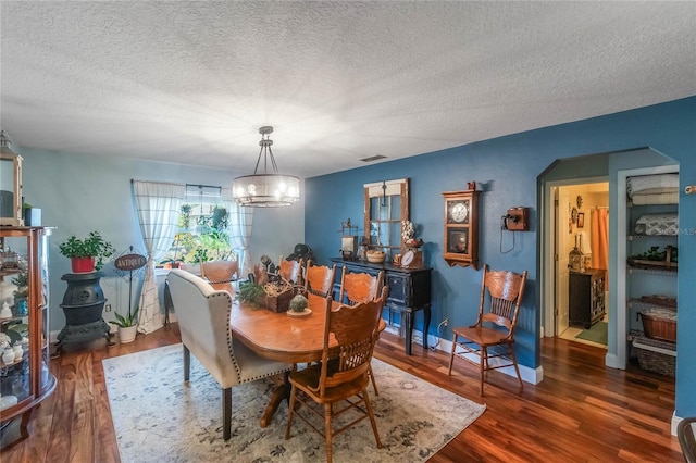 dining room featuring dark wood-type flooring, a textured ceiling, and an inviting chandelier