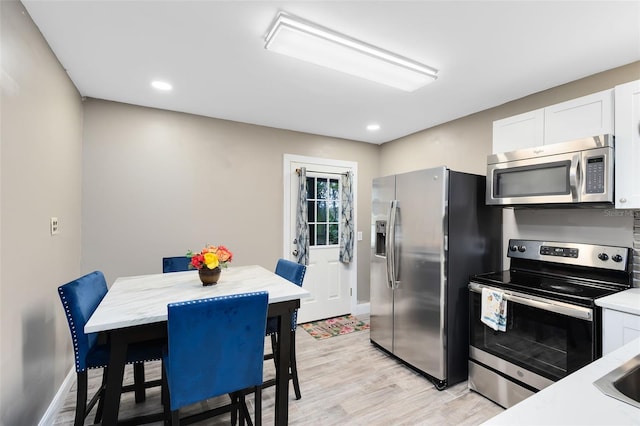 kitchen with light wood-type flooring, appliances with stainless steel finishes, and white cabinetry