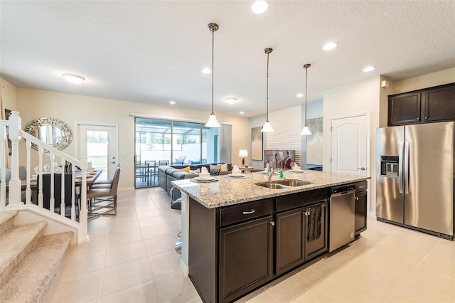 kitchen featuring light stone countertops, pendant lighting, stainless steel appliances, sink, and a kitchen island with sink