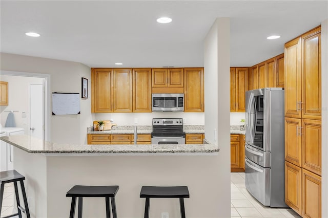 kitchen featuring a center island, light stone countertops, light tile patterned floors, a kitchen breakfast bar, and stainless steel appliances