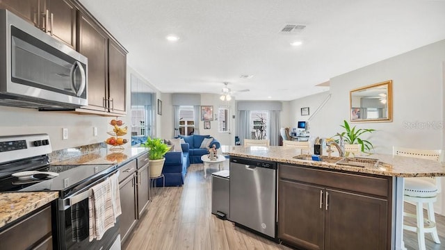 kitchen featuring a breakfast bar, dark brown cabinets, stainless steel appliances, light stone counters, and light wood-type flooring