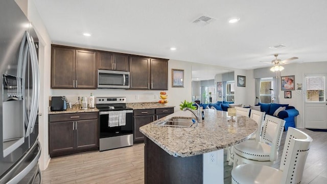 kitchen with light stone counters, stainless steel appliances, a kitchen island with sink, and sink