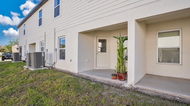 view of exterior entry with central AC, a patio, and a lawn