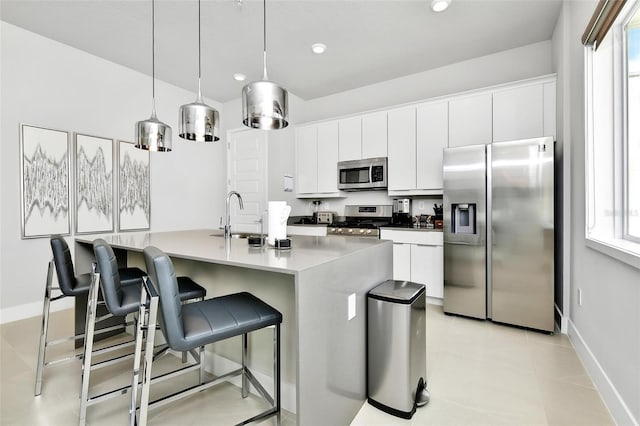 kitchen featuring sink, appliances with stainless steel finishes, white cabinetry, a center island with sink, and decorative light fixtures