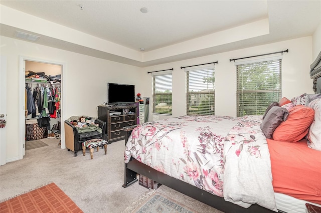 bedroom featuring a closet, a walk in closet, light colored carpet, and a tray ceiling