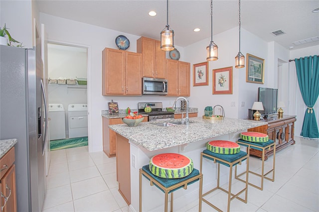 kitchen with light stone countertops, appliances with stainless steel finishes, washing machine and dryer, an island with sink, and a kitchen breakfast bar