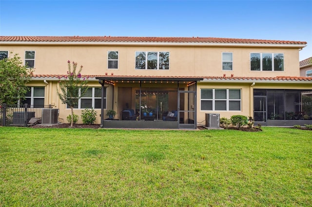 rear view of property with central air condition unit, a sunroom, and a lawn