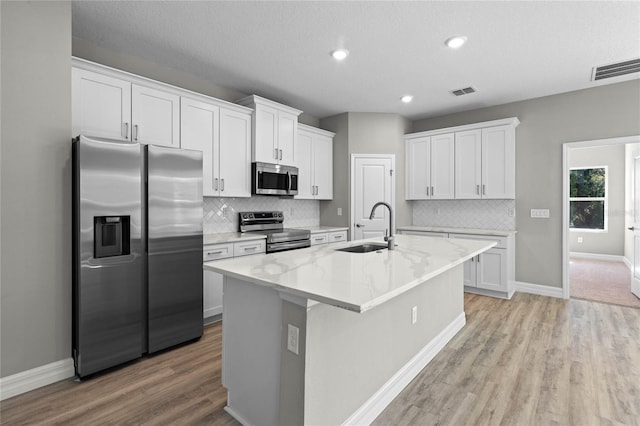 kitchen featuring appliances with stainless steel finishes, sink, white cabinetry, light stone counters, and a kitchen island with sink