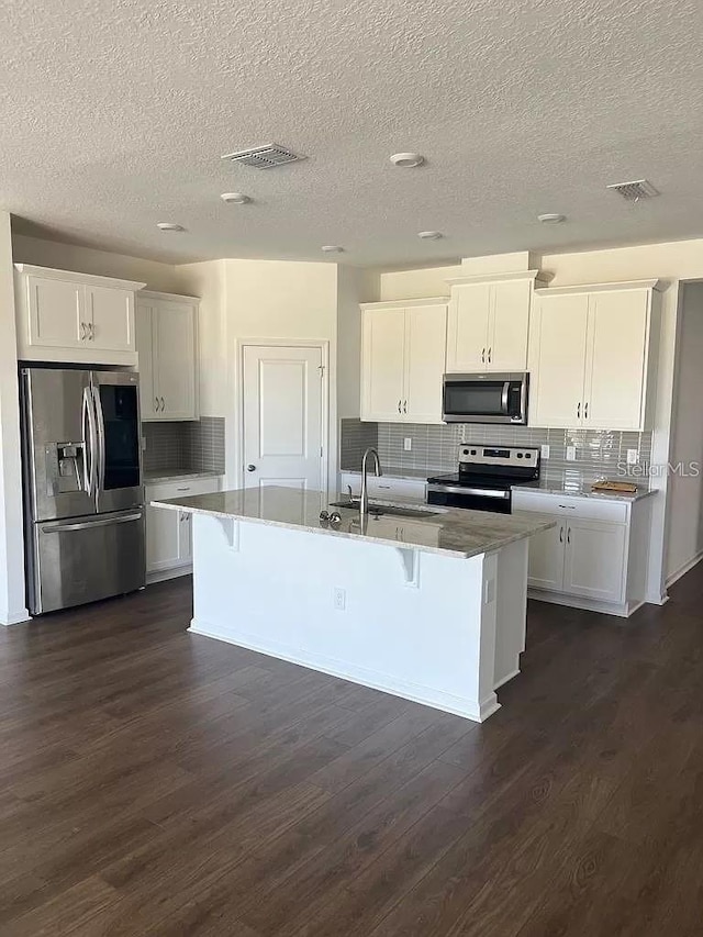 kitchen featuring white cabinetry, appliances with stainless steel finishes, a center island with sink, and a breakfast bar area