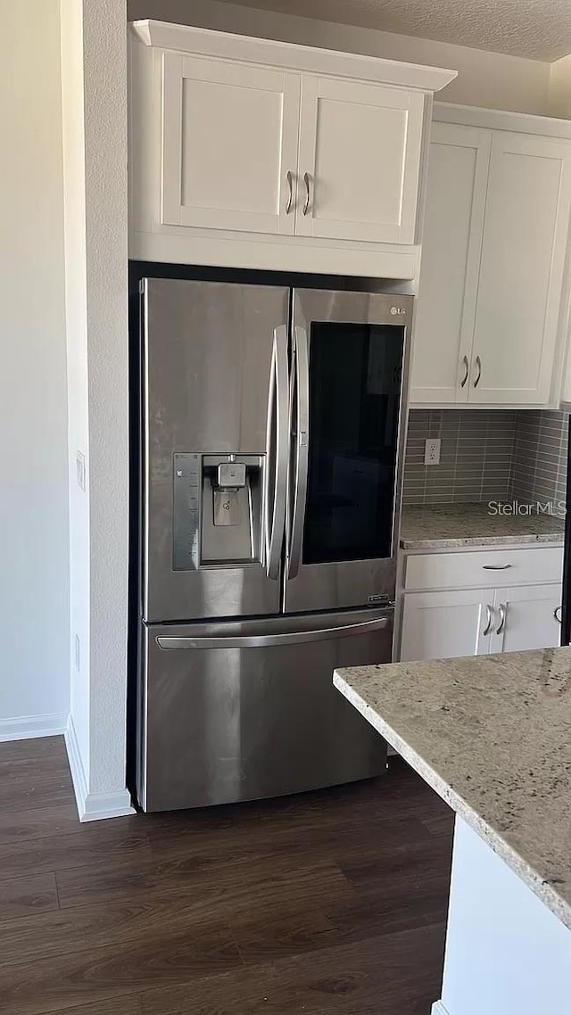 kitchen featuring backsplash, stainless steel refrigerator with ice dispenser, white cabinetry, dark hardwood / wood-style flooring, and light stone counters