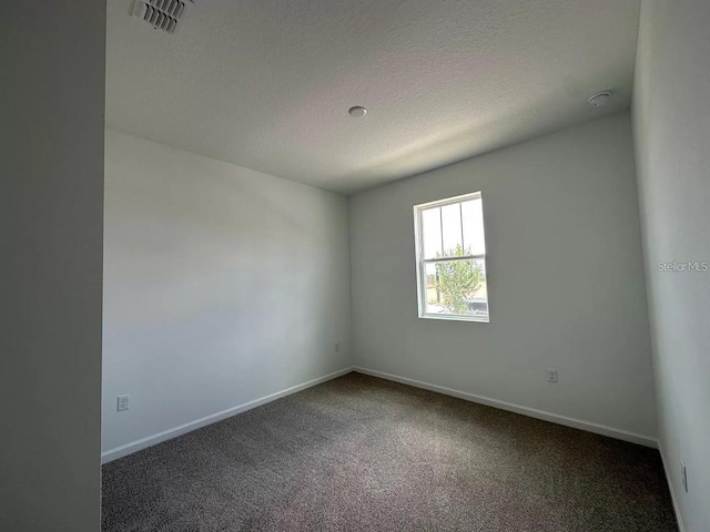 unfurnished room with a textured ceiling and dark colored carpet