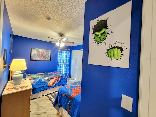 bedroom with a textured ceiling, ceiling fan, a closet, and light hardwood / wood-style flooring