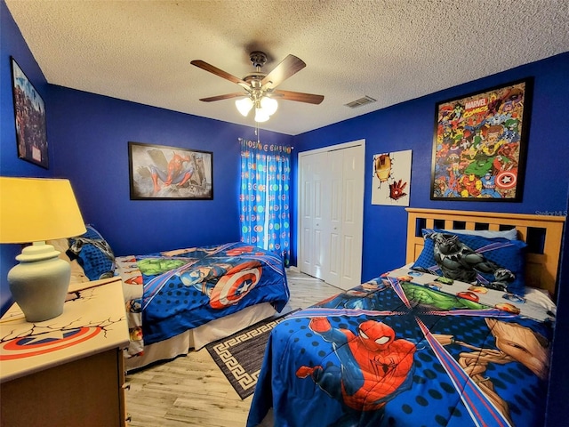 bedroom featuring a textured ceiling, a closet, light hardwood / wood-style floors, and ceiling fan