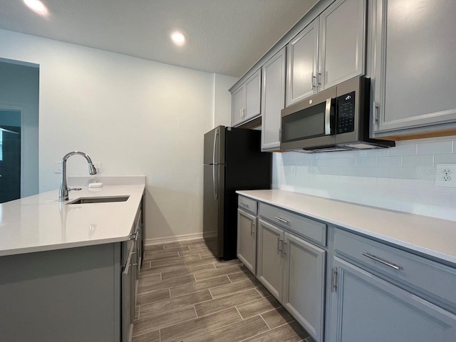 kitchen with decorative backsplash, sink, gray cabinets, and black fridge