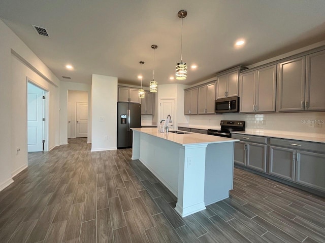 kitchen with electric stove, a center island with sink, black fridge, sink, and hanging light fixtures