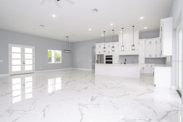 kitchen with decorative light fixtures, an island with sink, white cabinets, and appliances with stainless steel finishes