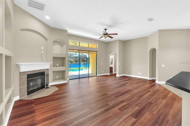 unfurnished living room with ceiling fan, hardwood / wood-style flooring, a tile fireplace, and built in shelves