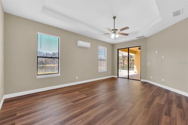 empty room featuring a raised ceiling, ceiling fan, dark wood-type flooring, and a wall mounted air conditioner