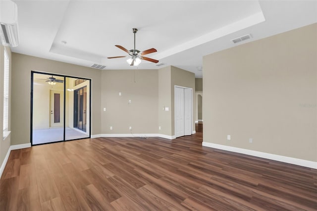 empty room with ceiling fan, dark wood-type flooring, and a tray ceiling