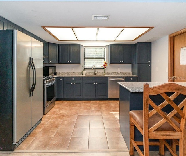 kitchen with appliances with stainless steel finishes, sink, light tile patterned flooring, light stone counters, and a breakfast bar