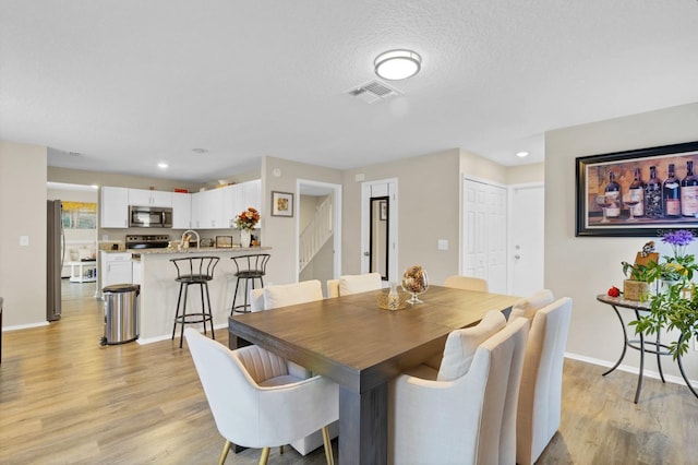 dining area with a textured ceiling, light hardwood / wood-style flooring, and sink